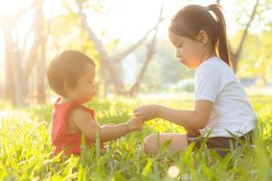 beau jeune enfant asiatique assis jouant en été dans le parc avec plaisir et gai sur l'herbe verte, activité des enfants avec détente et bonheur ensemble sur le pré, la famille et le concept de vacances. photo