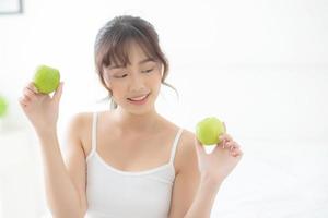 beau portrait jeune femme asiatique tenant et mangeant des pommes vertes dans la chambre à la maison, mode de vie de nutrition fille saine et soins perte de poids, concept de santé et de bien-être. photo