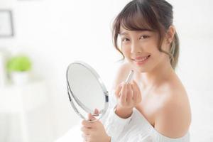 beau portrait jeune femme asiatique à la recherche d'un miroir appliquant du rouge à lèvres de maquillage dans la chambre, lèvres de beauté maquillage de fille d'asie et mode cosmétique sur la bouche à la maison, concept de mode de vie et de soins de santé. photo