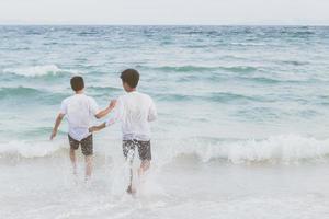 portrait homosexuel jeune couple asiatique courant avec gai ensemble sur la plage en été, asie gay faisant du tourisme pour les loisirs et se détendre avec bonheur en vacances en mer, concept juridique lgbt. photo