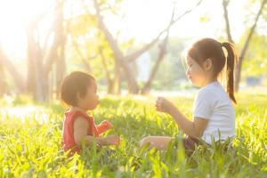 beau jeune enfant asiatique assis jouant en été dans le parc avec plaisir et gai sur l'herbe verte, activité des enfants avec détente et bonheur ensemble sur le pré, la famille et le concept de vacances. photo