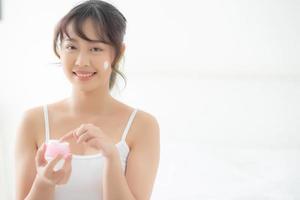 belle jeune femme asiatique heureuse d'appliquer une crème ou une lotion avec une crème hydratante sur le visage de la peau, beauté asie fille appliquant un soin du visage tactile avec maquillage cosmétique, concept de santé et de bien-être. photo