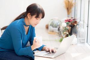 belle jeune femme asiatique indépendante souriante travaillant et sur un ordinateur portable au café du bureau avec une fille professionnelle, asiatique utilisant un ordinateur portable et buvant du café, des affaires et un concept de style de vie.