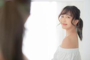 jeune femme asiatique souriante avec des vêtements essayant de s'habiller avec un miroir reflétant moderne et regardant dans la chambre, la fille choisit la mode des vêtements avec un concept de style de vie heureux et joyeux. photo