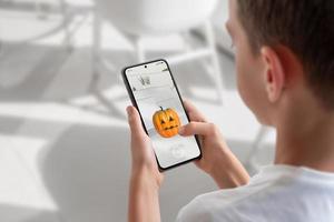 garçon sur un téléphone portable joue à un jeu de réalité augmentée. vue par-dessus l'épaule sur l'écran du téléphone. concept de jeu de lancer de citrouille photo