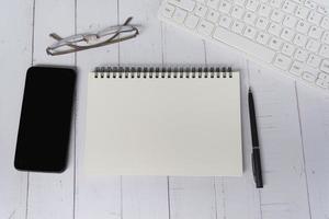 bloc-notes avec clavier d'ordinateur, smartphone, stylo et lunettes de lecture sur un bureau. photo