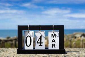 Texte de la date du calendrier 04 mars sur cadre en bois avec arrière-plan flou de l'océan. photo
