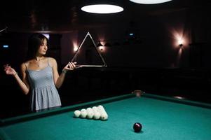 portrait d'une femme confuse posant avec un triangle au bord de la table de billard. photo