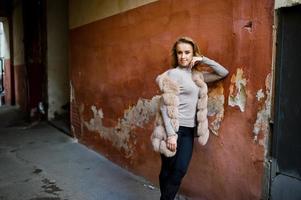 fille blonde au manteau de fourrure posé contre le vieux mur orange. photo