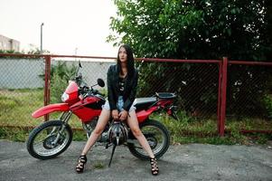 portrait d'une femme cool et géniale en robe et veste en cuir noir assise sur une moto rouge cool. photo