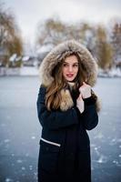 belle fille brune en vêtements chauds d'hiver. modèle sur la veste d'hiver contre le lac gelé au parc. photo