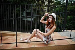étonnantes longues jambes avec des talons hauts fille portant un chapeau posant près des balustrades du bâtiment moderne. photo