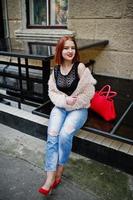 fille aux cheveux rouges avec sac à main rouge posé dans la rue de la ville. photo