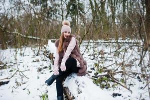 fille élégante en manteau de fourrure et couvre-chef à la forêt d'hiver. photo