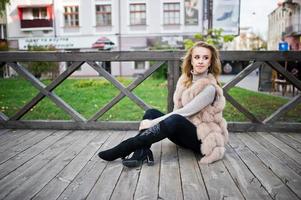 fille blonde au manteau de fourrure assis sur un plancher en bois à l'extérieur. photo