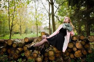 jeune fille blonde au manteau rose posé sur fond de souches de bois. photo