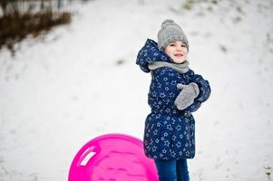 jolie petite fille avec des traîneaux de soucoupe à l'extérieur le jour de l'hiver. photo