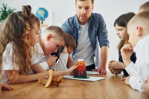 regardant le modèle de volcan. groupe d'enfants élèves en classe à l'école avec professeur photo