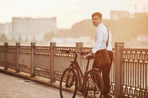 marchant avec son vélo près de la clôture. homme d'affaires en vêtements formels est dans la ville photo