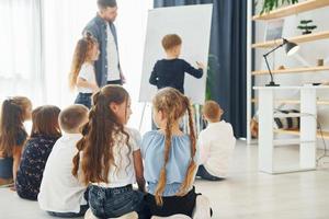 garçon écrivant au tableau. groupe d'enfants élèves en classe à l'école avec professeur photo