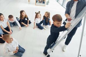 garçon écrivant au tableau. groupe d'enfants élèves en classe à l'école avec professeur photo