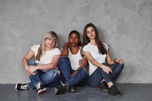 la fille afro-américaine est sérieuse. groupe de femmes multiethniques assises dans le studio sur fond gris photo