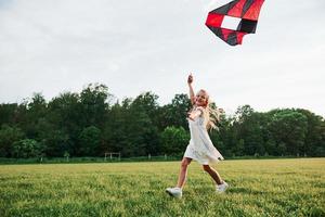 amusons nous ensemble. fille heureuse en vêtements blancs avec cerf-volant sur le terrain. belle nature photo