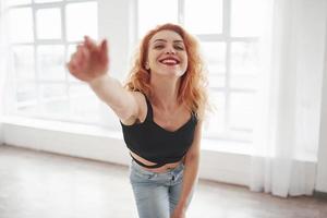 essayant de joindre le photographe. jolie femme rousse posant dans la chambre spacieuse près de la fenêtre photo