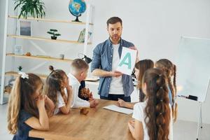 apprendre une nouvelle lettre. groupe d'enfants élèves en classe à l'école avec professeur photo