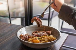 riz frit à l'ail gras de boeuf avec steak de boeuf et garniture de jaune d'oeuf mariné dans un bol sur une table en bois. viandes grillées photo