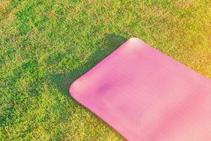 tapis de yoga rose posé sur l'herbe verte dans le parc le soir il y avait une douce lumière du soleil. les tons clairs chauds conviennent aux exercices de yoga. photo
