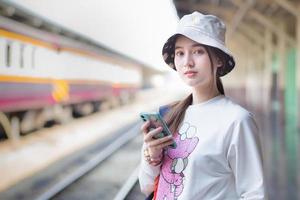 belle femme asiatique tenant un sac et un smartphone à la recherche d'informations de voyage. en attendant le train sur le quai. photo