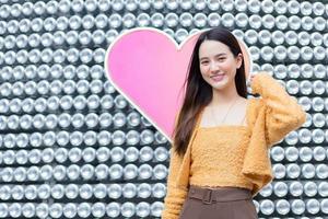 belle femme asiatique aux cheveux longs est debout et souriant sur fond de coeur comme concept de la saint-valentin. fond abstrait photo