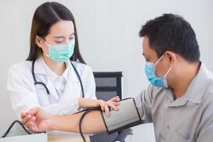 une femme médecin asiatique professionnelle utilise un tensiomètre avec un homme patient pour vérifier sa santé à l'hôpital. ils portent un masque médical pour protéger l'infection du système respiratoire. photo