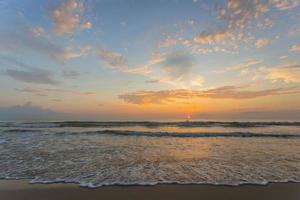 la mer baigne la plage de sable au coucher du soleil. ciel orange bleu avec fond de vue sur la mer. photo