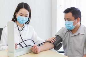 une femme médecin asiatique utilise un tensiomètre avec un homme patient pour vérifier sa santé à l'hôpital. ils portent un masque médical pour protéger l'infection du système respiratoire. photo