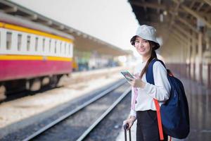 belle femme asiatique porte un sac et un smartphone à la recherche d'informations de voyage. en attendant le train sur le quai photo