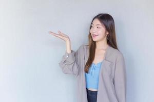 belle jeune femme asiatique aux longs cheveux bruns dans une chemise bleue agit à la main comme présentant quelque chose sur le fond. photo