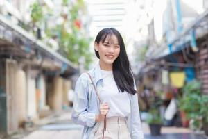 une jeune femme asiatique confiante qui porte une chemise et un sac bleu blanc sourit joyeusement et regarde la caméra alors qu'elle se rend au travail dans la vieille ville. photo