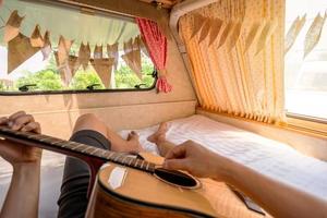 jeune homme voyageur allongé dans un camping-car et jouant de la guitare pendant un voyage sur la route en vacances photo