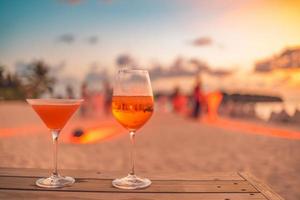 deux cocktails avec des fêtards flous sur la plage et un ciel coloré au coucher du soleil en arrière-plan. mode de vie de loisirs en plein air de luxe, couleurs relaxantes et romantiques, personnes floues faisant la fête un soir d'été