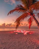 dîner romantique sur la plage avec coucher de soleil, bougies aux feuilles de palmier et ciel et mer au coucher du soleil. vue imprenable, paysage de lune de miel ou de dîner d'anniversaire. horizon de soirée île exotique, romance pour un couple photo