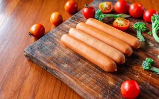 saucisse crue sur une planche à découper en bois avec brocoli et tomates photo