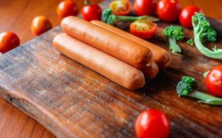 saucisse crue sur une planche à découper en bois avec brocoli et tomates photo