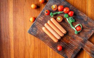 saucisse crue sur une planche à découper en bois avec brocoli et tomates photo