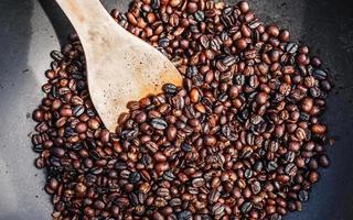 torréfaction traditionnelle des grains de café dans une poêle en métal avec une cuillère en bois photo