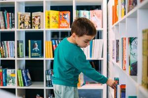 un petit garçon cherche une étagère de livres pour enfants dans la librairie. photo