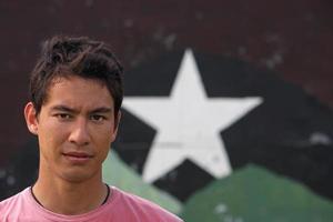 jeune adulte eurasien regardant dans l'appareil photo avec un regard confiant et sérieux, tout en se tenant devant un mur avec une étoile dessus.