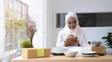 jeune femme musulmane professionnelle et prospère propriétaire d'une petite entreprise parlant au téléphone avec son client et notant une commande sur le bloc-notes. photo