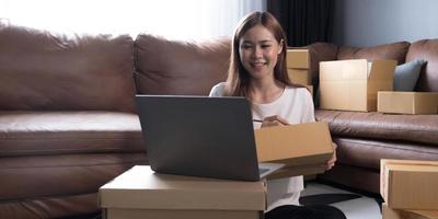 expédition des achats en ligne, jeune propriétaire de petite entreprise en démarrage écrivant une adresse sur une boîte en carton sur le lieu de travail. entrepreneur de petite entreprise PME ou femme asiatique indépendante travaillant avec une boîte à la maison photo